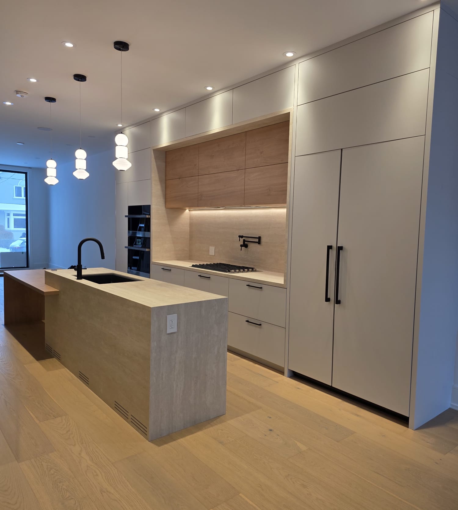 Completed kitchen with light cabinetry, wood-look upper cabinets, a large island and black fixtures.