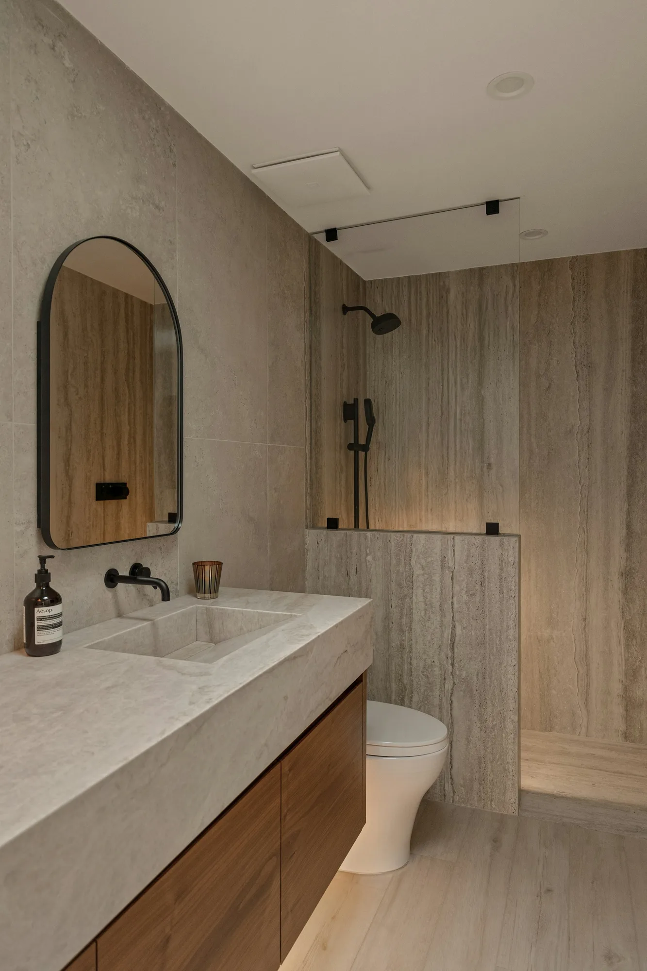 Modern bathroom with a stone countertop, floating wood vanity and walk-in shower