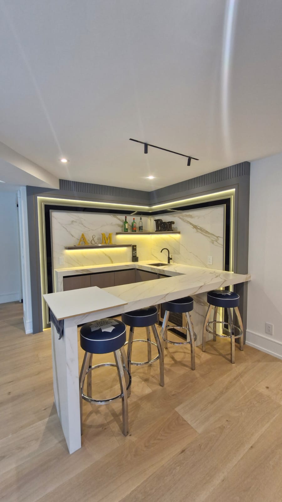 Corner bar with a white veined counter, four stools, open shelves and warm accent lighting